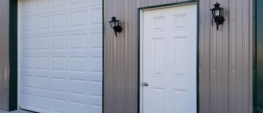 There are two garage doors and two doors on the side of a building.