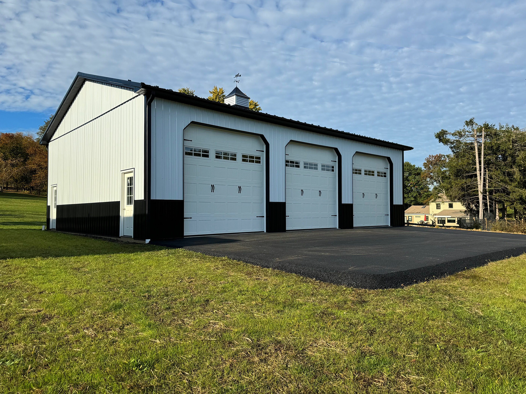A white and black garage with three garage doors is sitting in the middle of a grassy field.