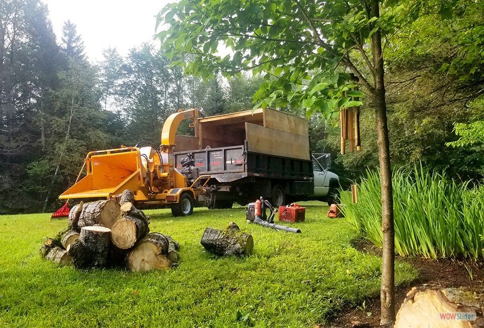 Un broyeur d'arbres est garé dans l'herbe à côté d'un camion à benne basculante.