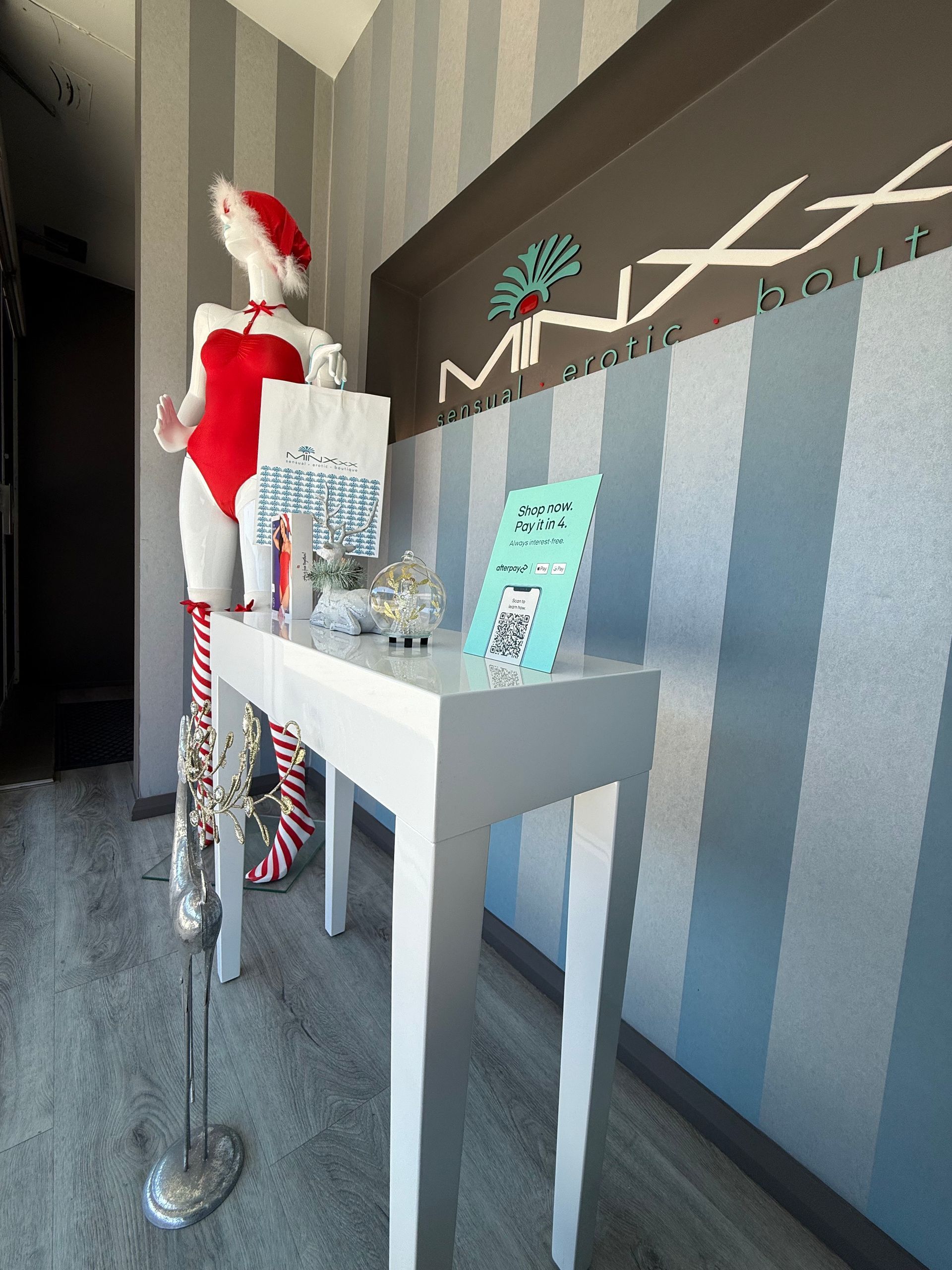 Mannequin in Santa hat and red bodysuit, white table with brochures, striped wall.