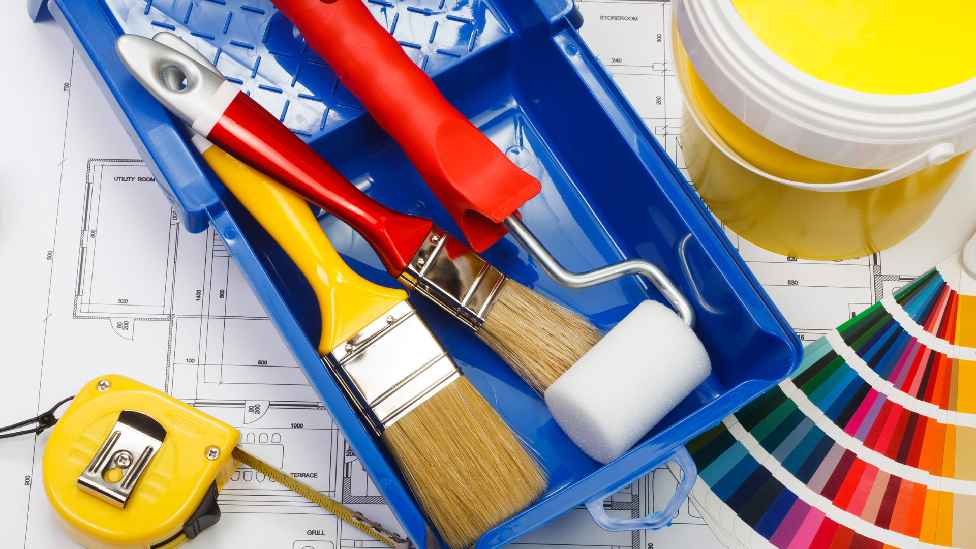 Paint tools, including brushes, rollers, tape measure, paint can, and color swatches, on a blueprint.
