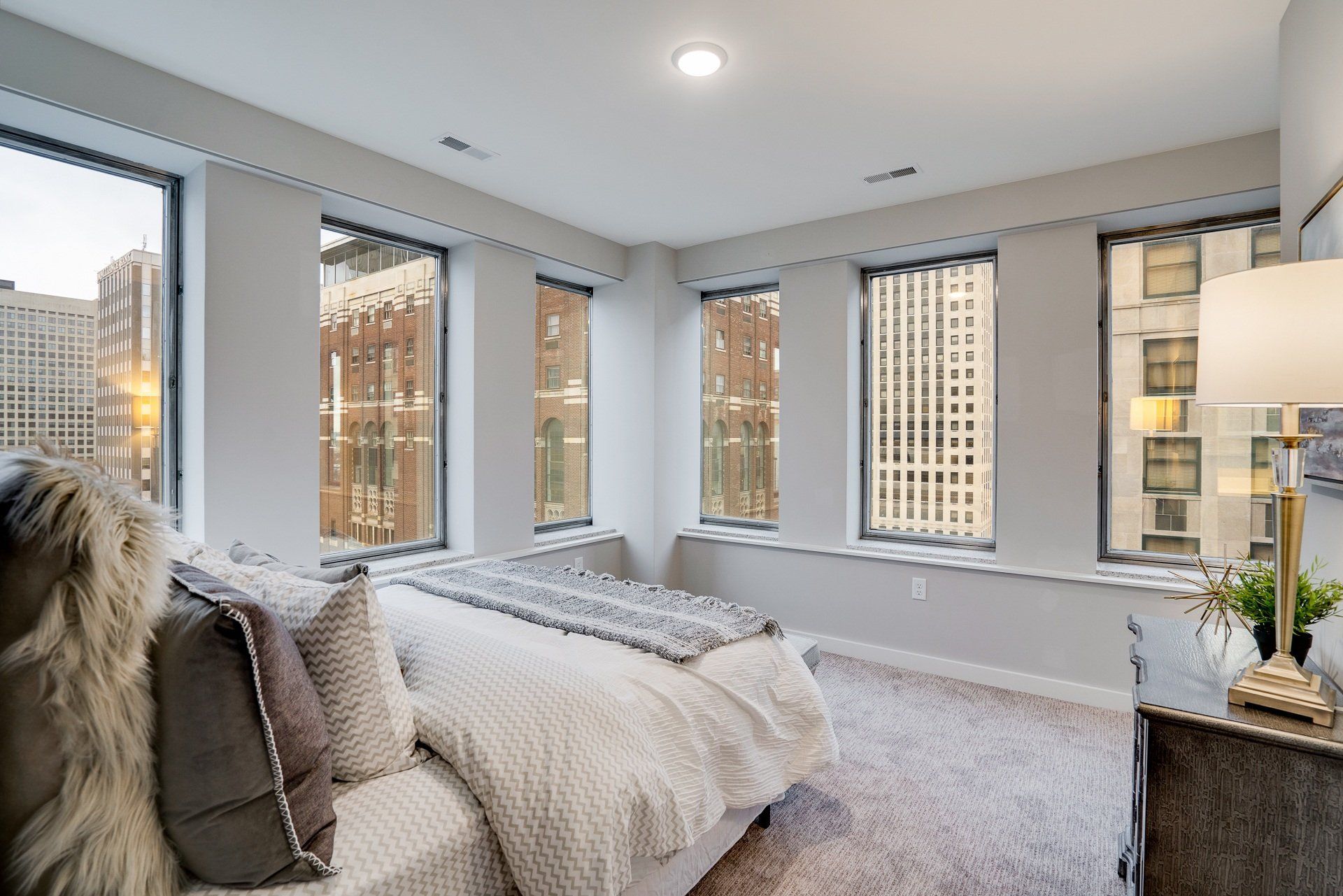 Bright bedroom in a high-rise apartment with large windows and city views.