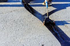 A person is spreading black paint on a concrete surface.