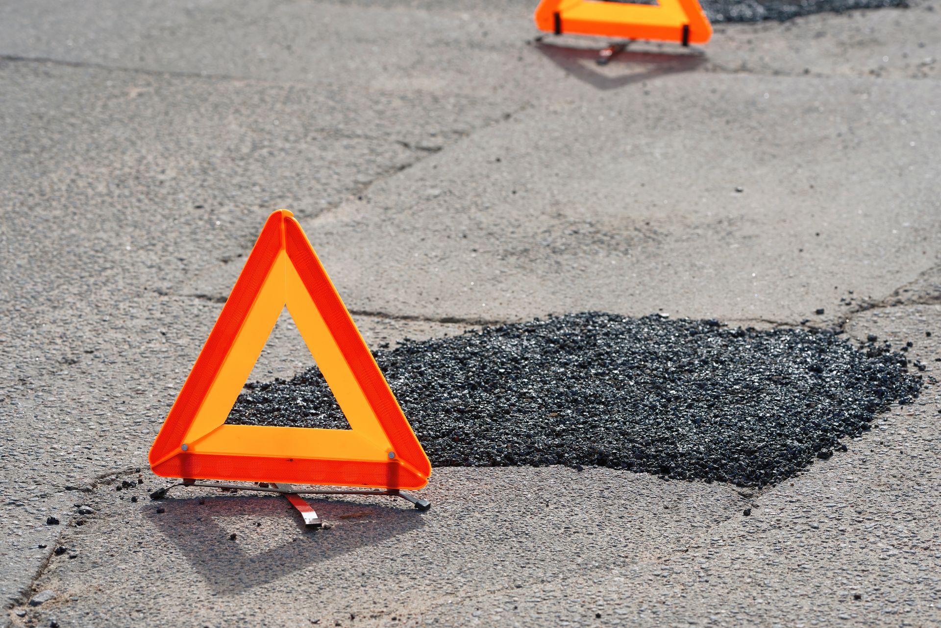 A warning triangle is sitting on the side of the road next to a pothole.