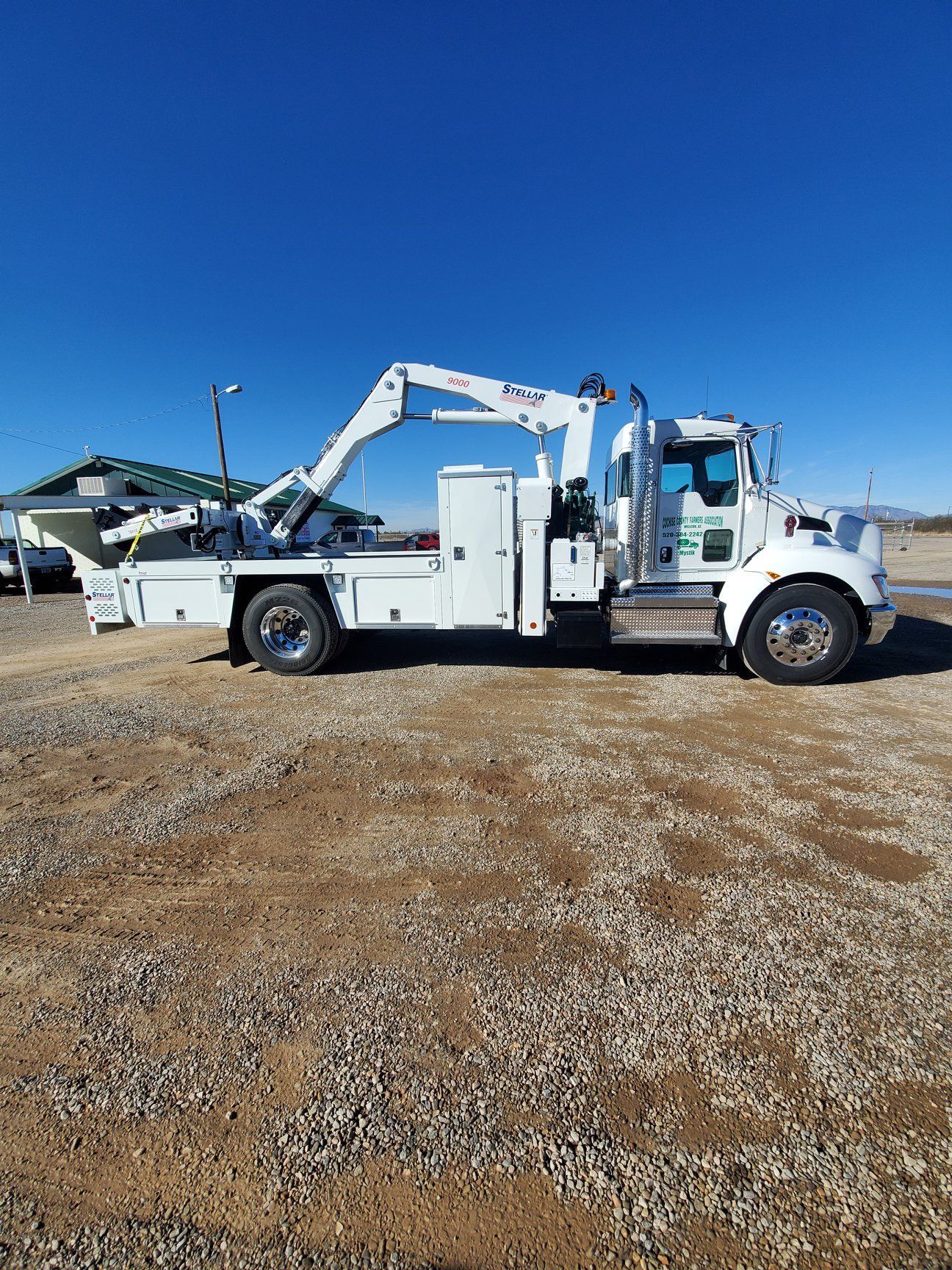 a white tow truck with a crane attached to it is parked in a gravel lot .