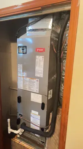 A Bryant air handler unit installed in a closet with visible ductwork and a white PVC drain pipe at the base.