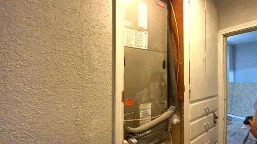 A metal HVAC furnace unit installed in an open wall alcove next to a set of wooden drawers and a doorway.