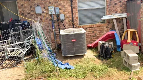 An outdoor area against a brick wall featuring an HVAC unit, children's plastic play equipment, and metal patio chairs.