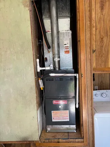 A Goodman furnace installed in a narrow closet space next to a washing machine.