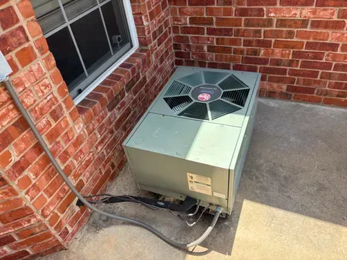 A light green, rectangular air conditioning unit sitting on a concrete patio next to a red brick wall.