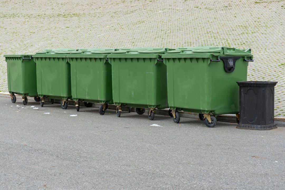 A Row of Green Garbage Cans Are Lined Up in a Parking Lot — Anderson Waste Services in Bowral, NSW