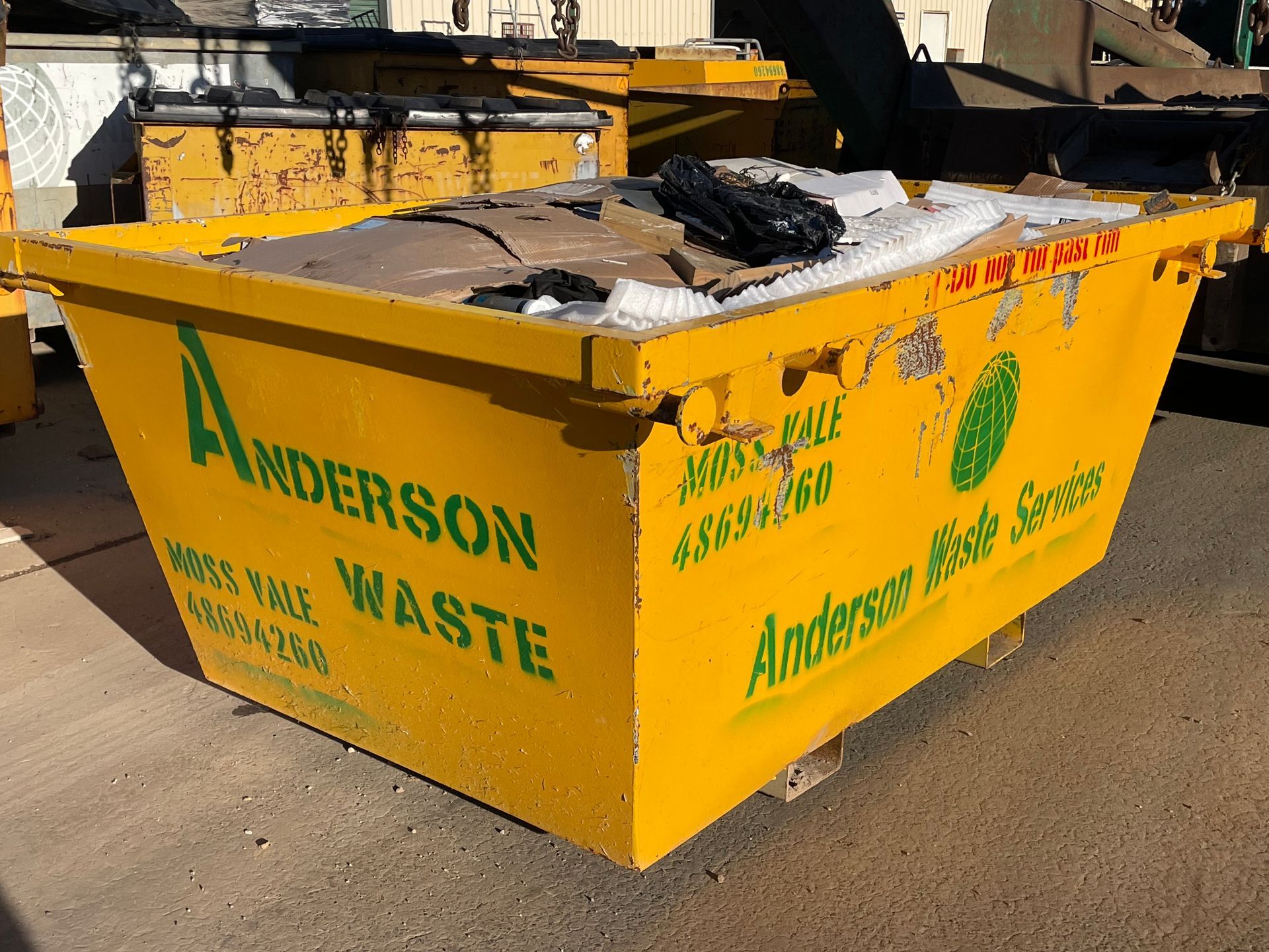 A Yellow Dumpster is Parked in Front of a Brick House — Anderson Waste Services in Bowral, NSW