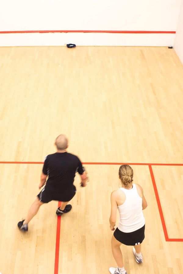 A man and a woman are playing squash on a court