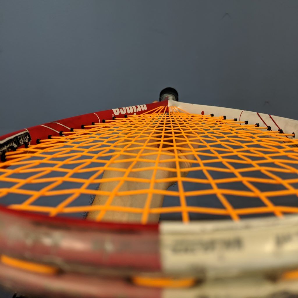 Tennis racket with orange strings and red and white frame.