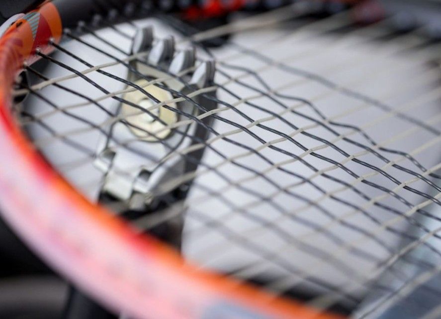 A close up of a badminton racket with orange strings