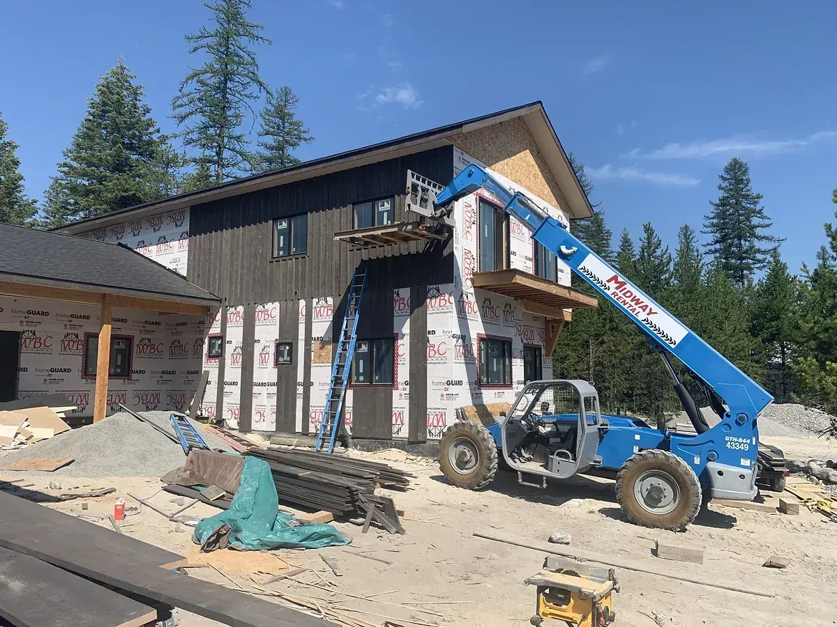 A blue forklift is parked in front of a house under construction.