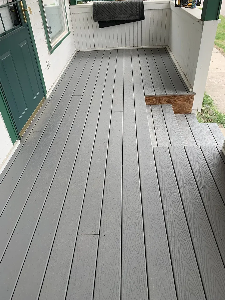 A porch with a gray wooden floor and a green door.