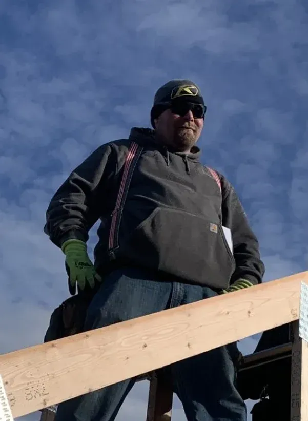 A man wearing a black jacket and a hat is standing on a wooden railing.