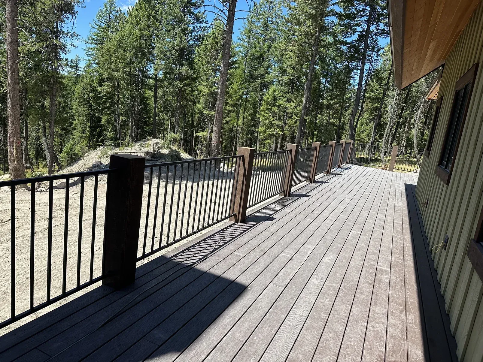 A large wooden deck with a metal railing and trees in the background.