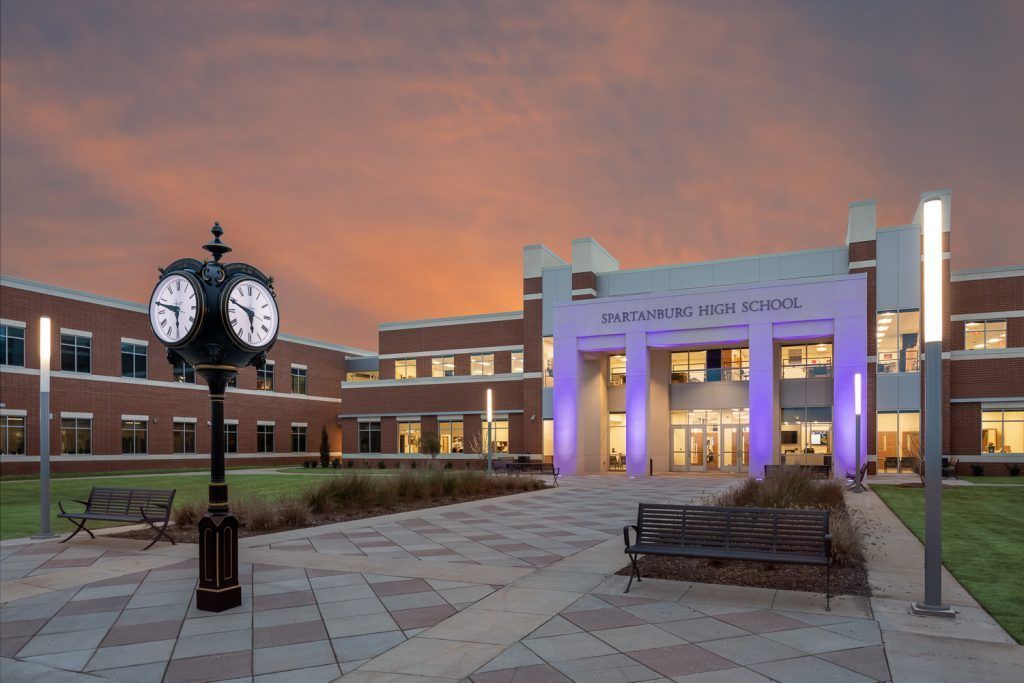 A large building, illuminated by purple lighting with a clock in front of it