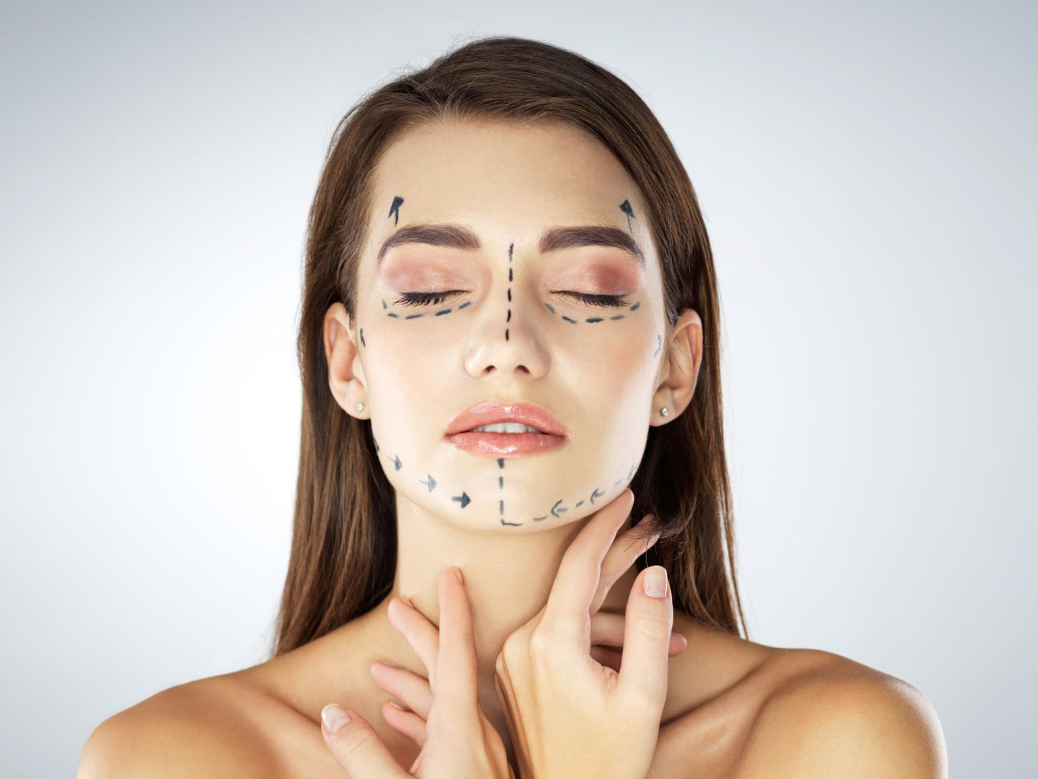 Woman with surgical markings on face, eyes closed, hands near neck.