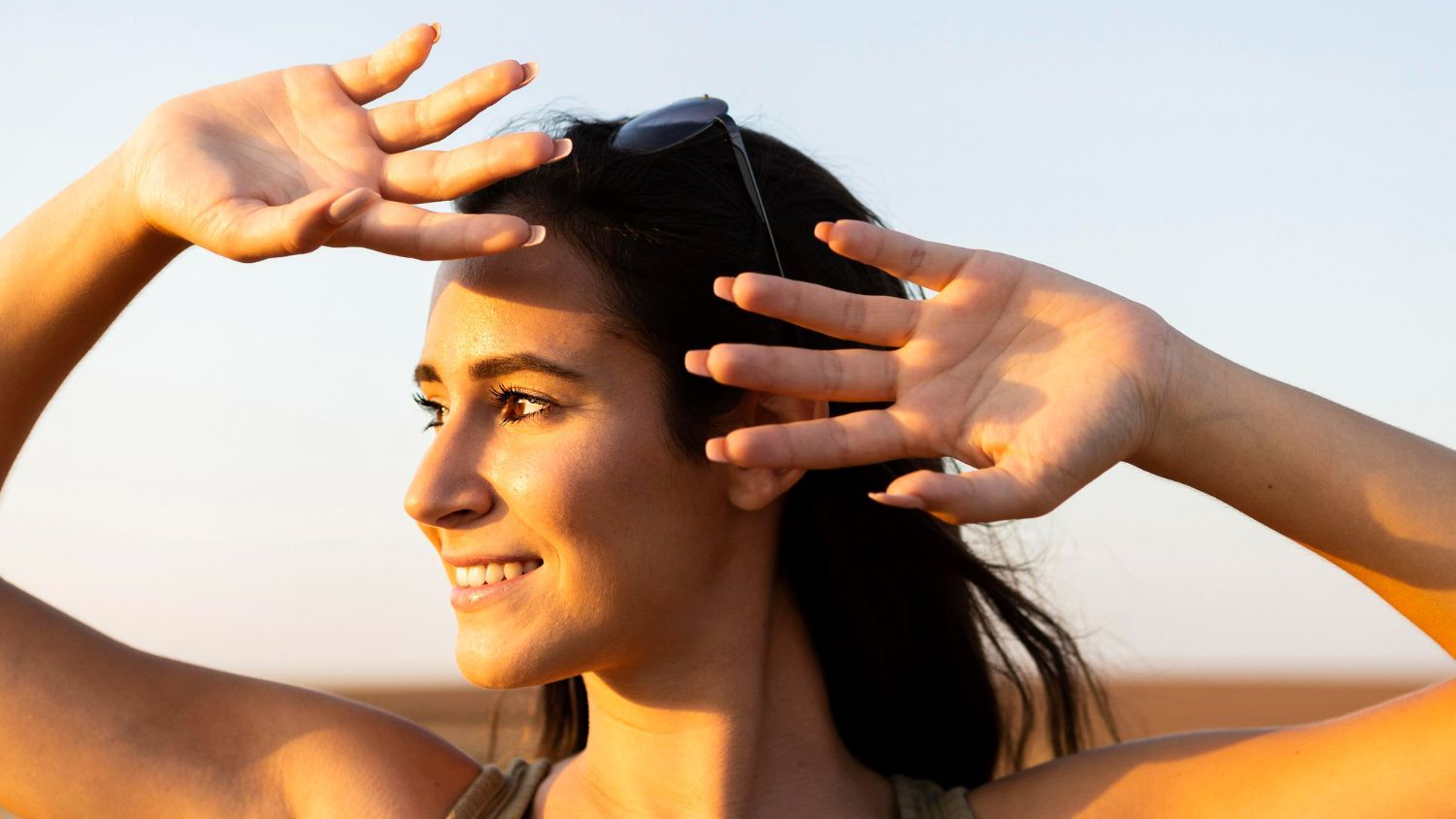 A woman is covering her eyes from the sun with her hands.