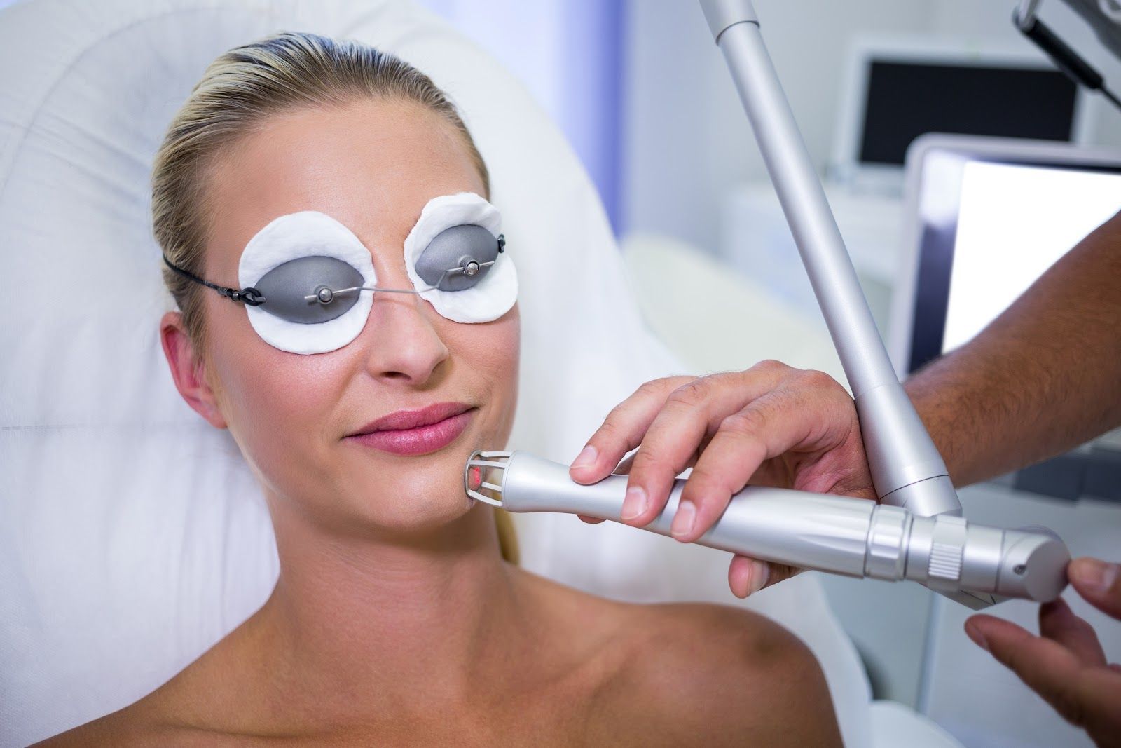 Woman receiving facial laser treatment, wearing eye protection, in a medical setting.