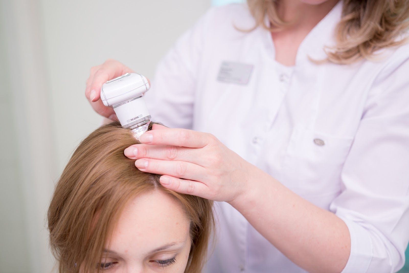 Woman receiving scalp treatment with a handheld device in a medical setting.