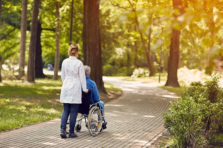 nurse helping elderly man on wheelchair outdoor. 
