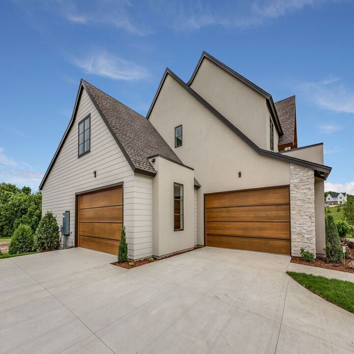 Modern two-story house with a concrete driveway, brown garage doors, and a beige exterior under a blue sky.
