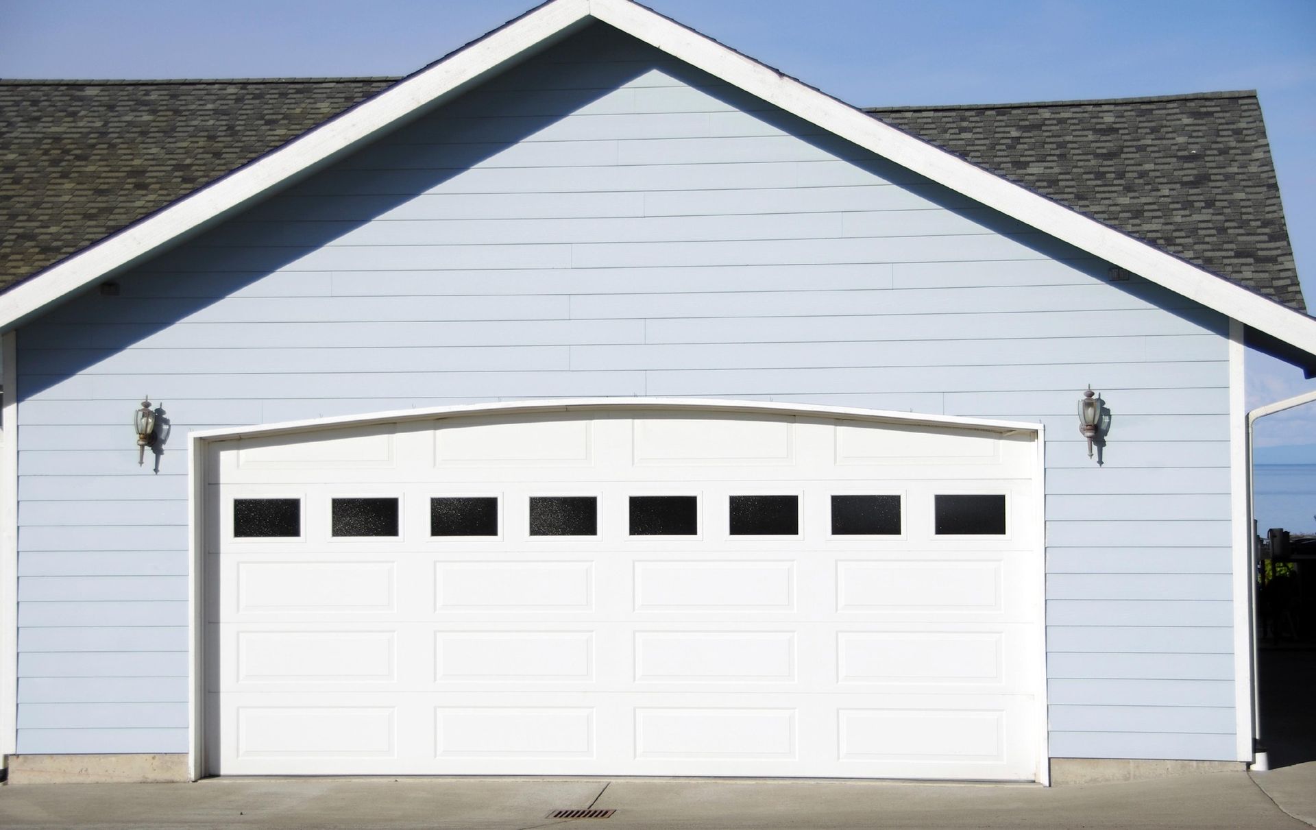 White garage door on a light blue building, arched top with windows.