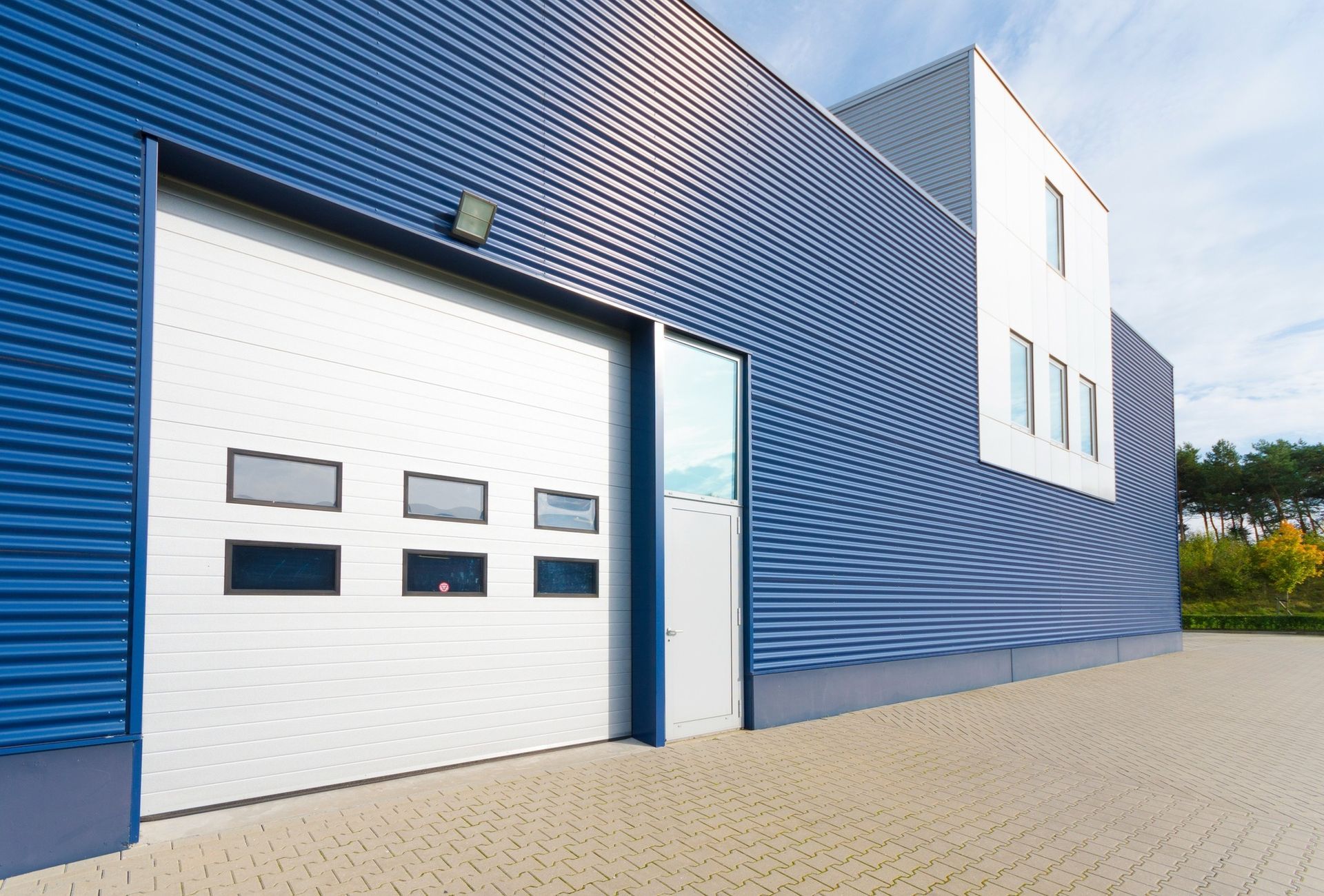 Blue industrial building with large garage door and rectangular windows.
