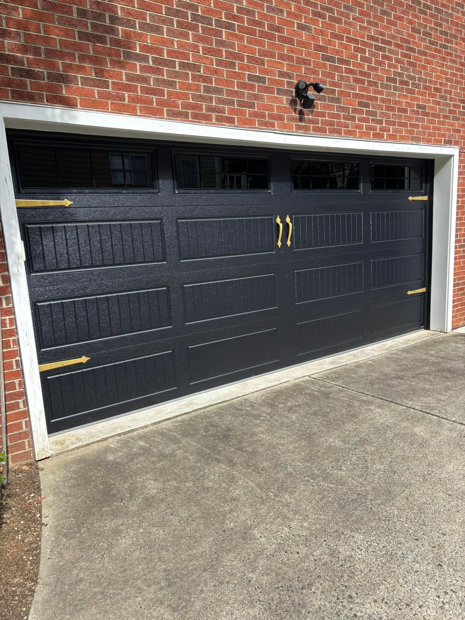 Black garage door with gold hardware against a brick building. White trim surrounds the door.