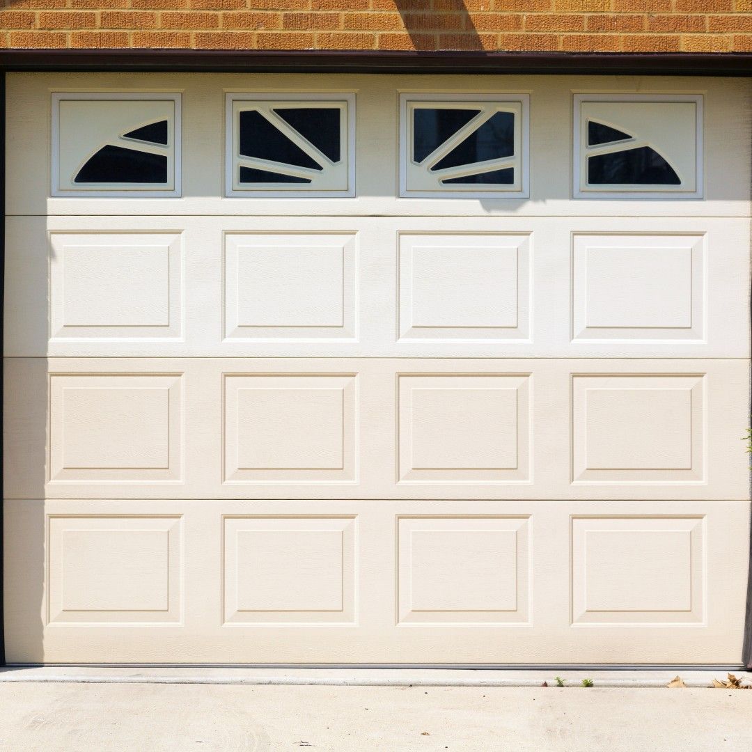 White garage door with four windows at the top, brick wall above, and concrete driveway below.