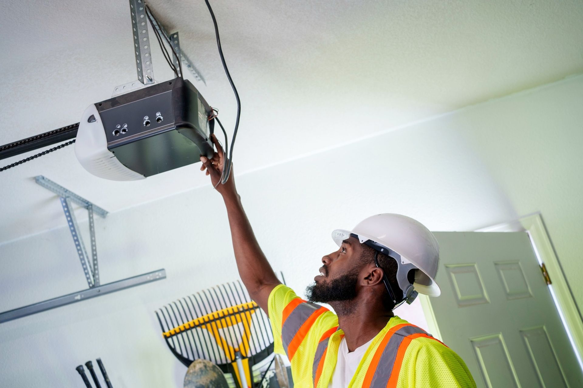 Man in hard hat and safety vest repairs garage door opener.