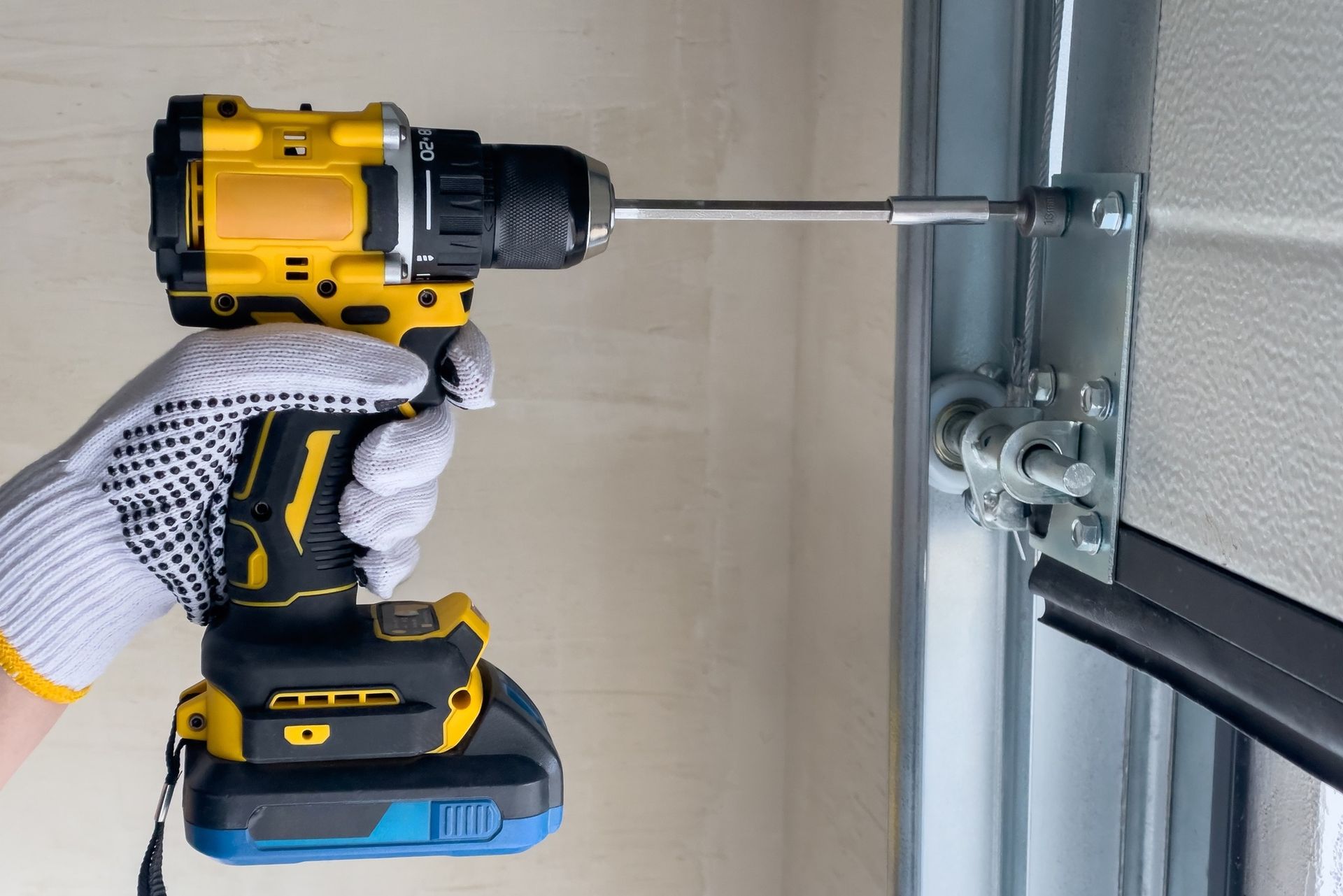 Person wearing work gloves using a yellow and black drill to screw into a garage door frame.