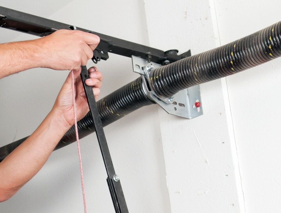 Person using tools to adjust a garage door spring system.