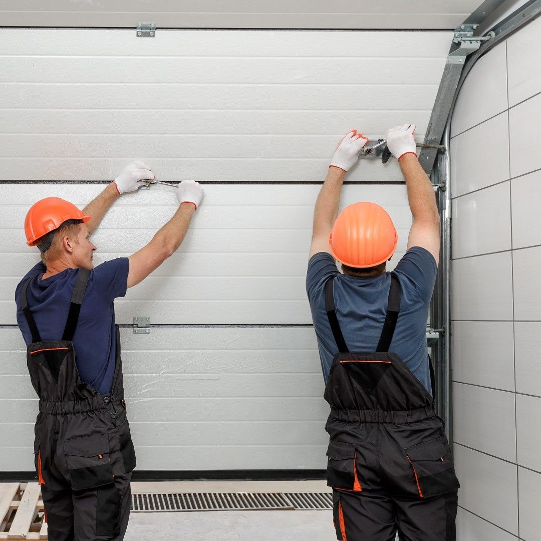 Two workers in orange hard hats and overalls installing a garage door.