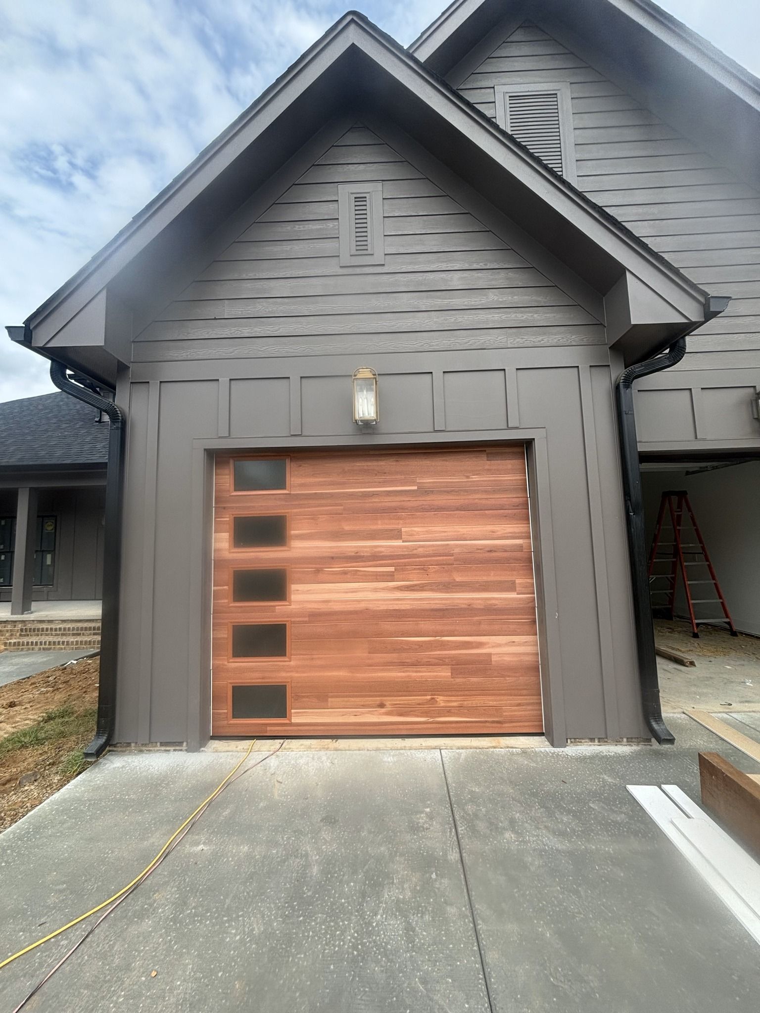 Garage with wood door and windows, brown and gray siding, concrete driveway.