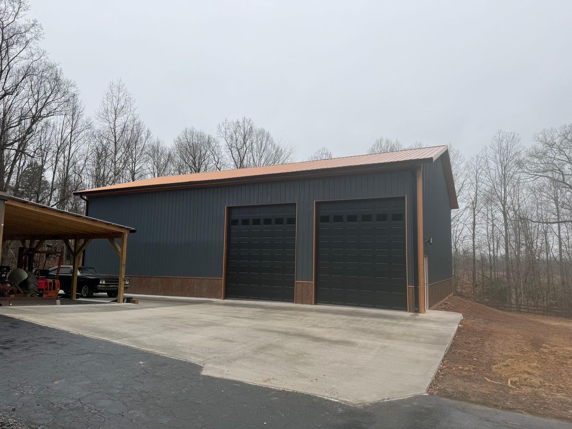 Two-car garage with dark gray siding, black doors, brown trim, and copper-colored roof. A concrete driveway is in front.
