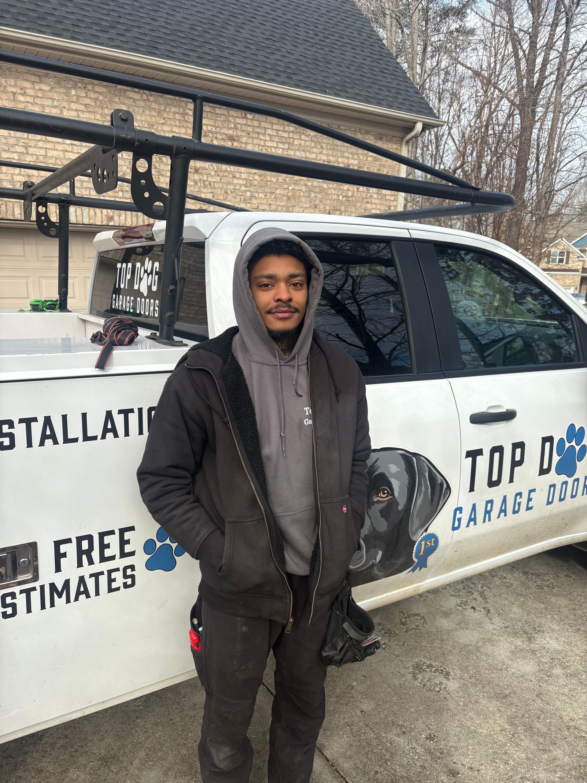 Man standing by a truck with a logo for Top Dog Garage Doors; he is wearing a jacket and a hoodie.