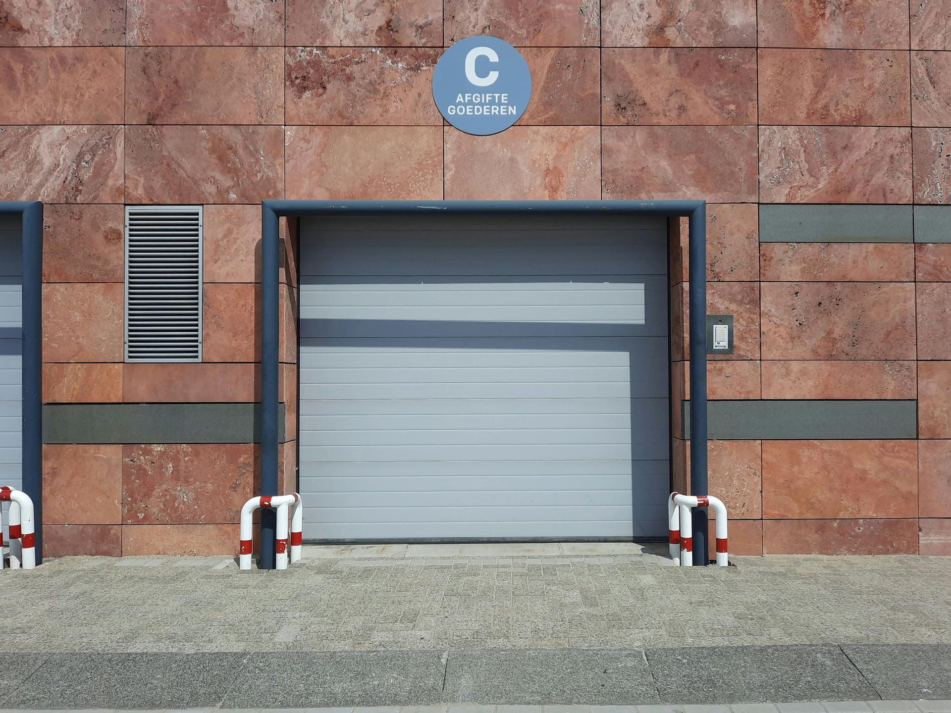 Gray garage door in a red-brown brick building. Above the door is a blue sign with a white 