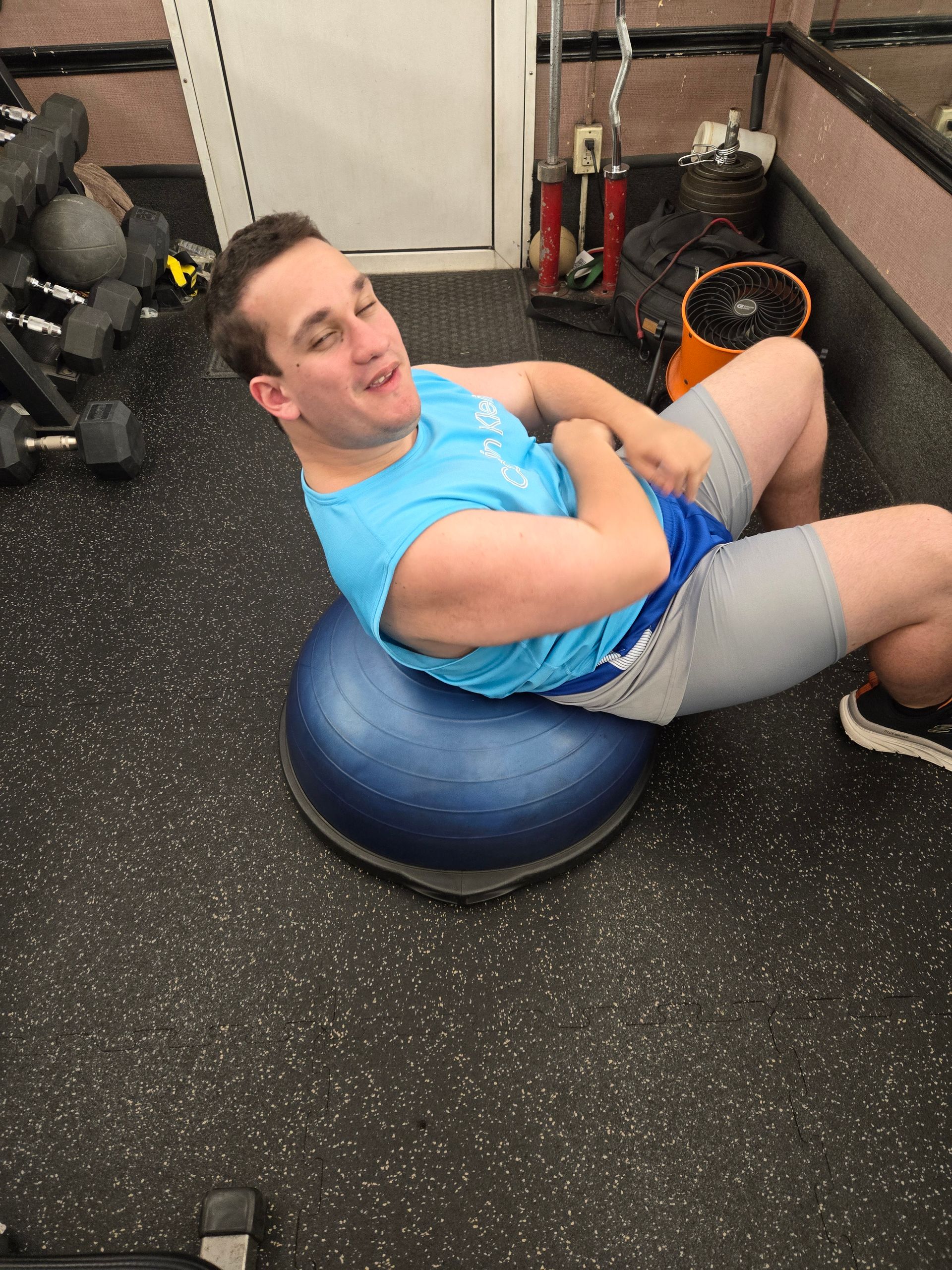 A man is sitting on a blue exercise ball in a gym