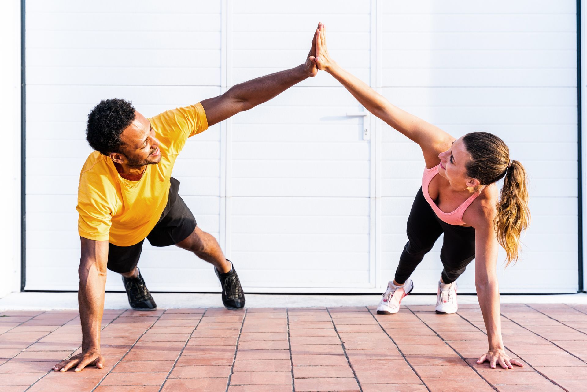 A man and a woman are doing push ups and giving each other a high five.