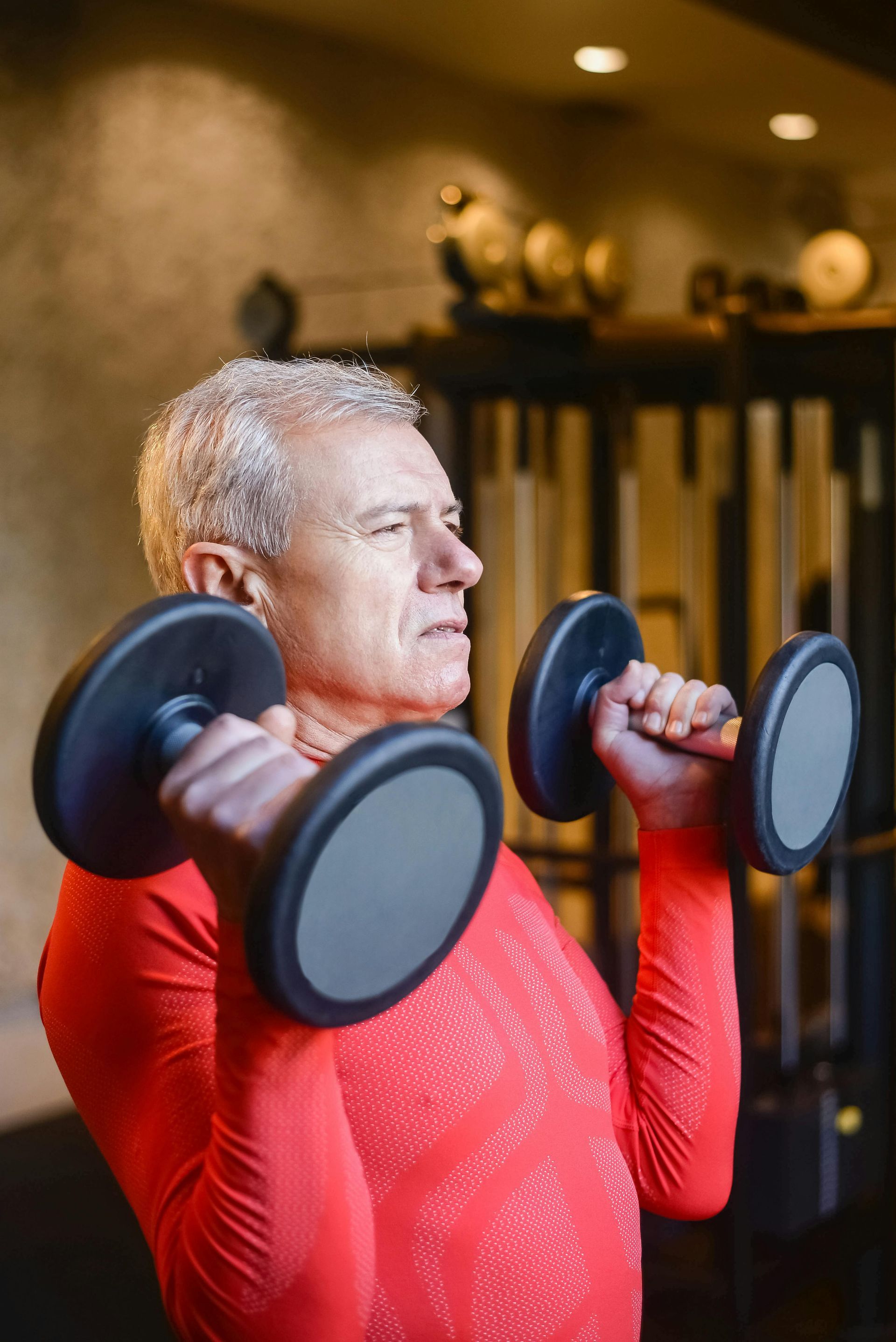 An older man is lifting dumbbells in a gym.