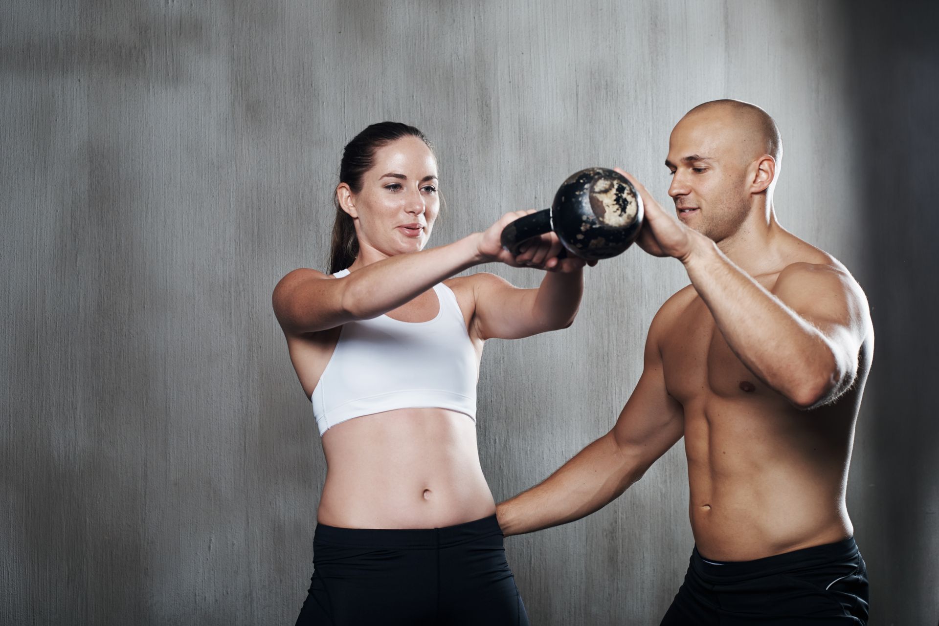 A man is helping a woman lift a kettlebell.