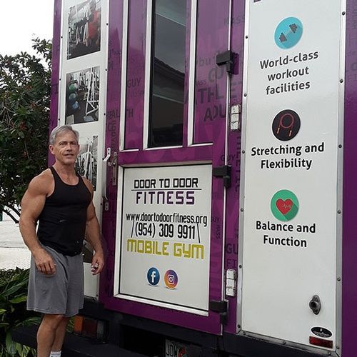 A man is standing in front of a purple mobile gym truck.