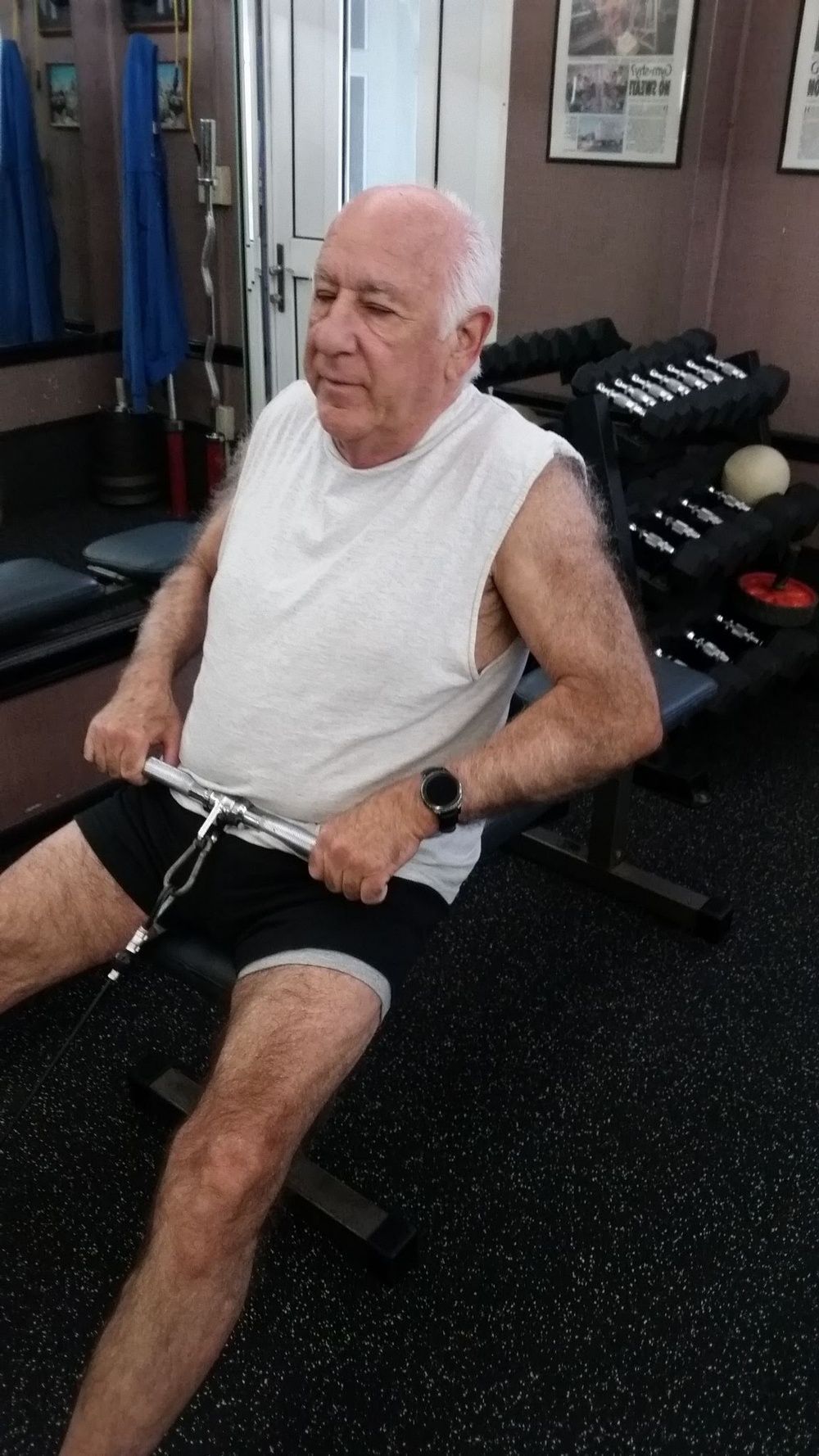 An older man is sitting on a rowing machine in a gym.