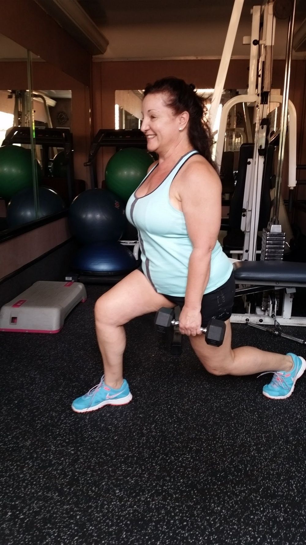 A woman is doing lunges with a dumbbell in a gym