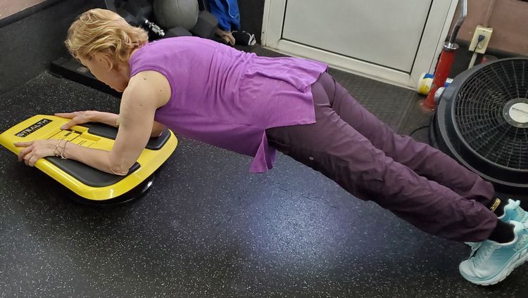 A woman in a purple shirt is doing a plank on a yellow board.